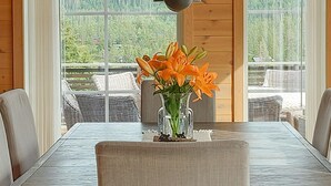 Ein Esstisch mit einer Vase mit orangefarbenen Lilien, Holzvertäfelung und Korbmöbeln.