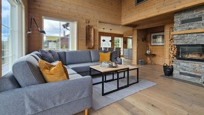 Ein modernes Wohnzimmer mit einem grauen Ecksofa, einem Holztisch und einem Kamin aus Stein.