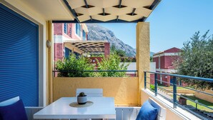 Un balcón con una mesa y sillas blancas, vista a edificios y una montaña al fondo.