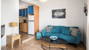 A compact living space with a kitchenette, a sofa, a coffee table, and a wall-mounted artwork. - Akti Barbati Houses by Konnect - Two-Bedroom Maisonette (Corfu)