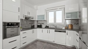 A modern kitchen with white cabinets, stainless steel appliances, and a marble backsplash.