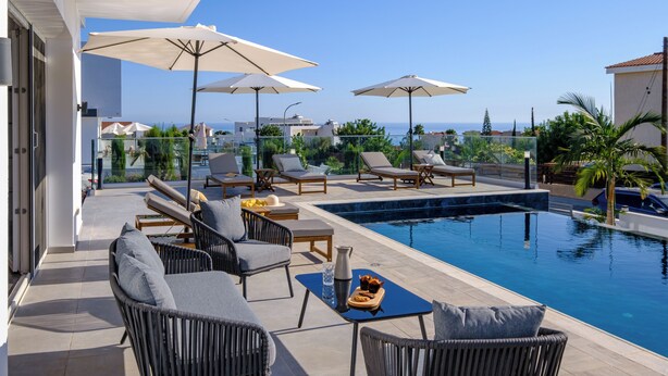 A poolside area with lounge chairs, umbrellas, and a clear view of the sea.