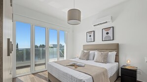 A modern bedroom with a large bed, a nightstand, and a sliding glass door leading to a balcony.