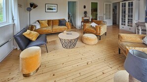 A spacious living room with a wooden floor, a sofa set, a round coffee table, and a cabinet with glass doors.