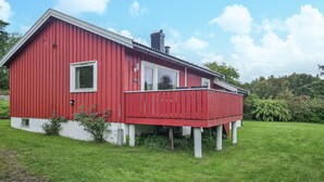 A red wooden house with a white porch, a chimney, and a small window.