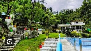 A building with a white exterior, surrounded by lush greenery and a stone staircase leading up to it. - Song Valley Resort By Blue Waves (Dehradun)