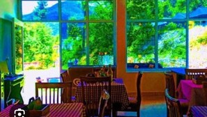 A room with large windows, a ceiling fan, and a table with chairs. - Song Valley Resort By Blue Waves (Dehradun)