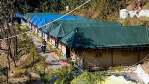 Uma fileira de edifícios baixos e simples, com lonas verdes sobre os telhados, provavelmente estruturas temporárias.
