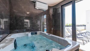 A modern bathroom with a jacuzzi, dark marble walls, and a glass door leading to a pool area. - Luxurious home in Razanac (Razanac)