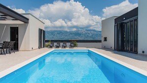 A modern outdoor swimming pool with a mountain view, surrounded by lounge chairs and a table. - Luxurious home in Razanac (Razanac)