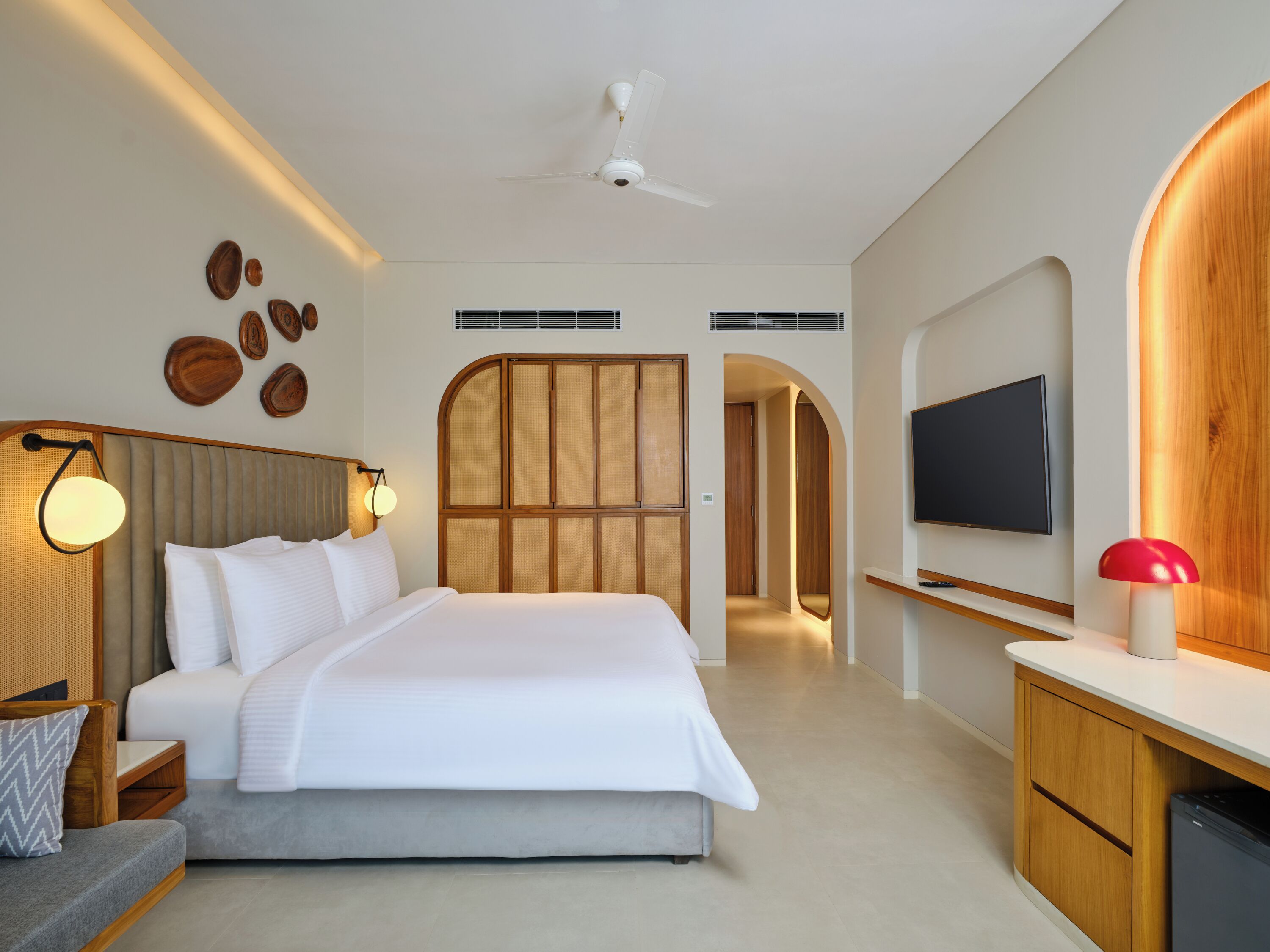 Una habitación de hotel moderna con una cama grande, televisión, escritorio y ventilador de techo.