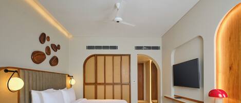 Una habitación de hotel moderna con una cama grande, televisión, escritorio y ventilador de techo.