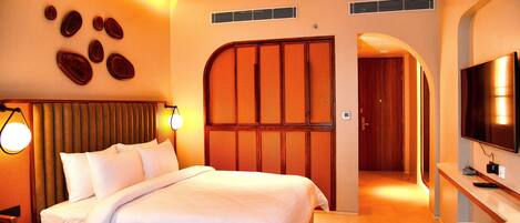 A hotel room with a large bed, a TV, a desk, and a wall with decorative elements.