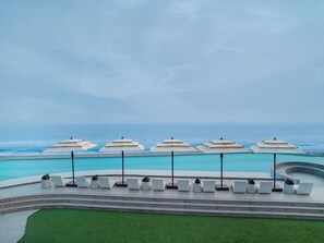 A poolside area with lounge chairs and umbrellas, overlooking a clear blue ocean. - Swosti Premium Beach Resorts Puri (Brahmagiri)