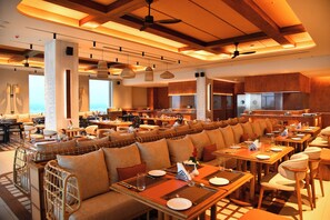 A spacious restaurant with high ceilings, wooden beams, and a long dining area with booths and tables. - Swosti Premium Beach Resorts Puri (Brahmagiri)