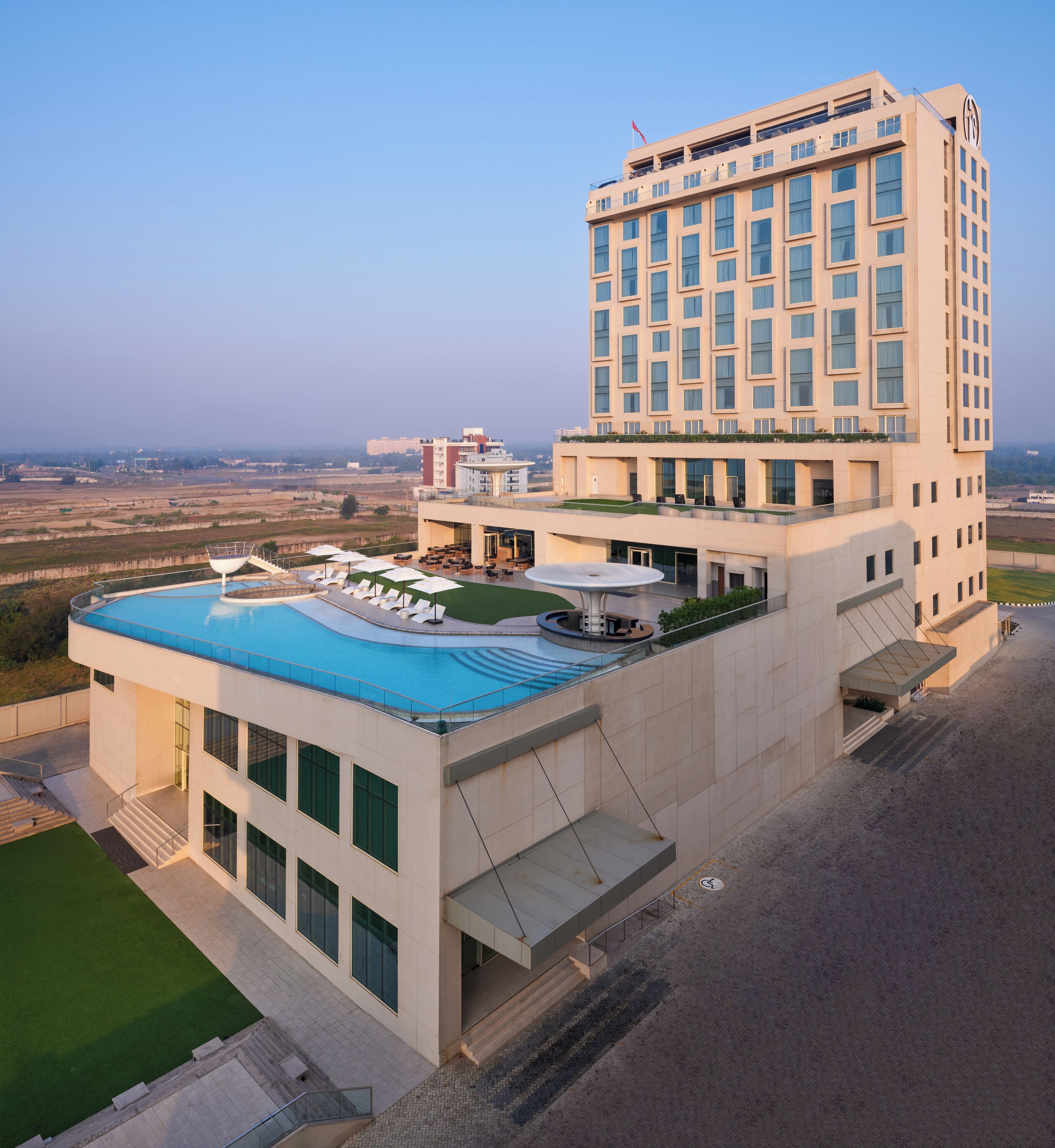 A modern hotel with a rooftop pool, a large building with multiple floors, and a view of the surrounding landscape.