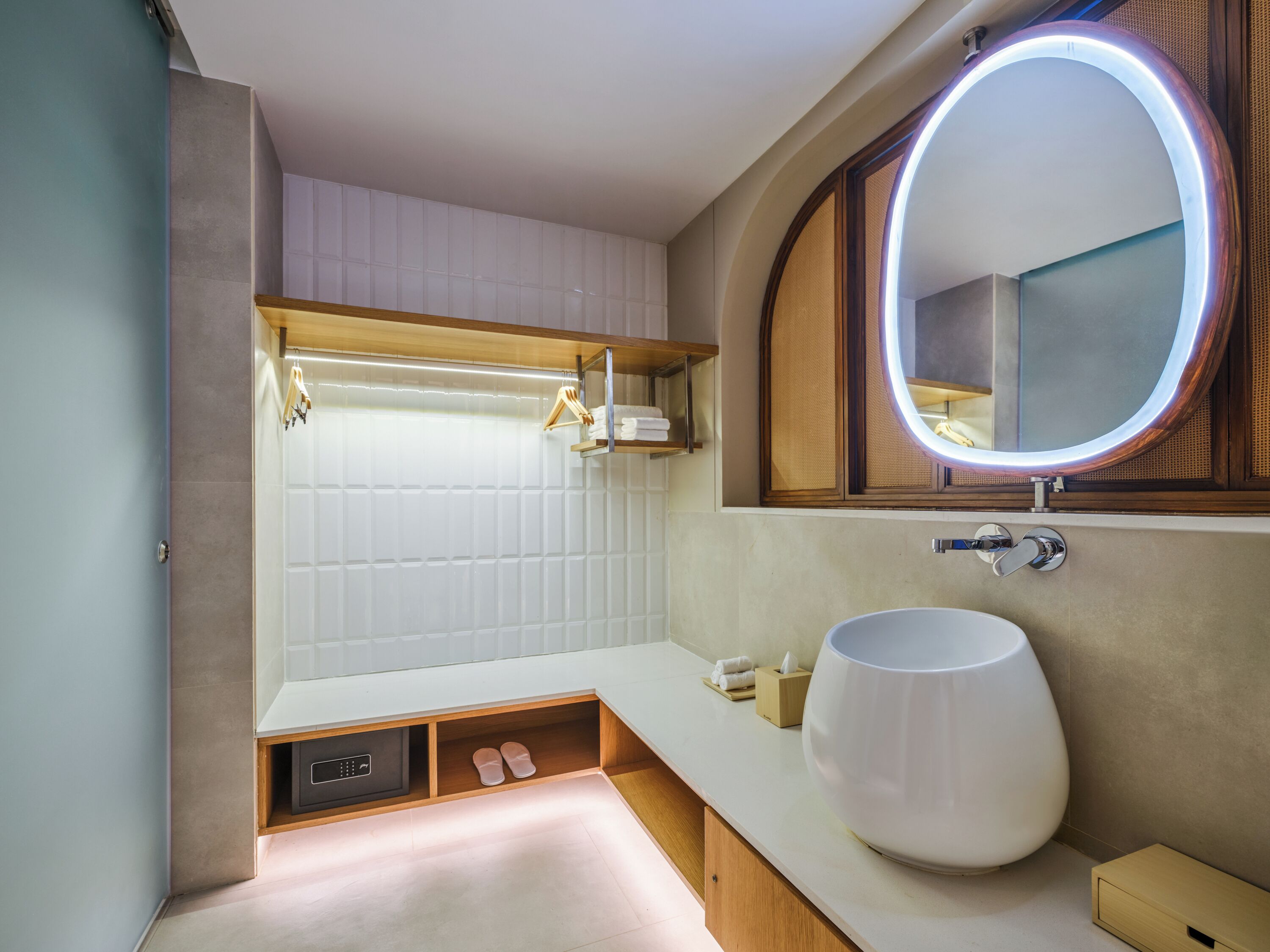 A modern bathroom with a large oval sink, a built-in mirror with LED lighting, a towel rack, and a built-in shoe storage area.