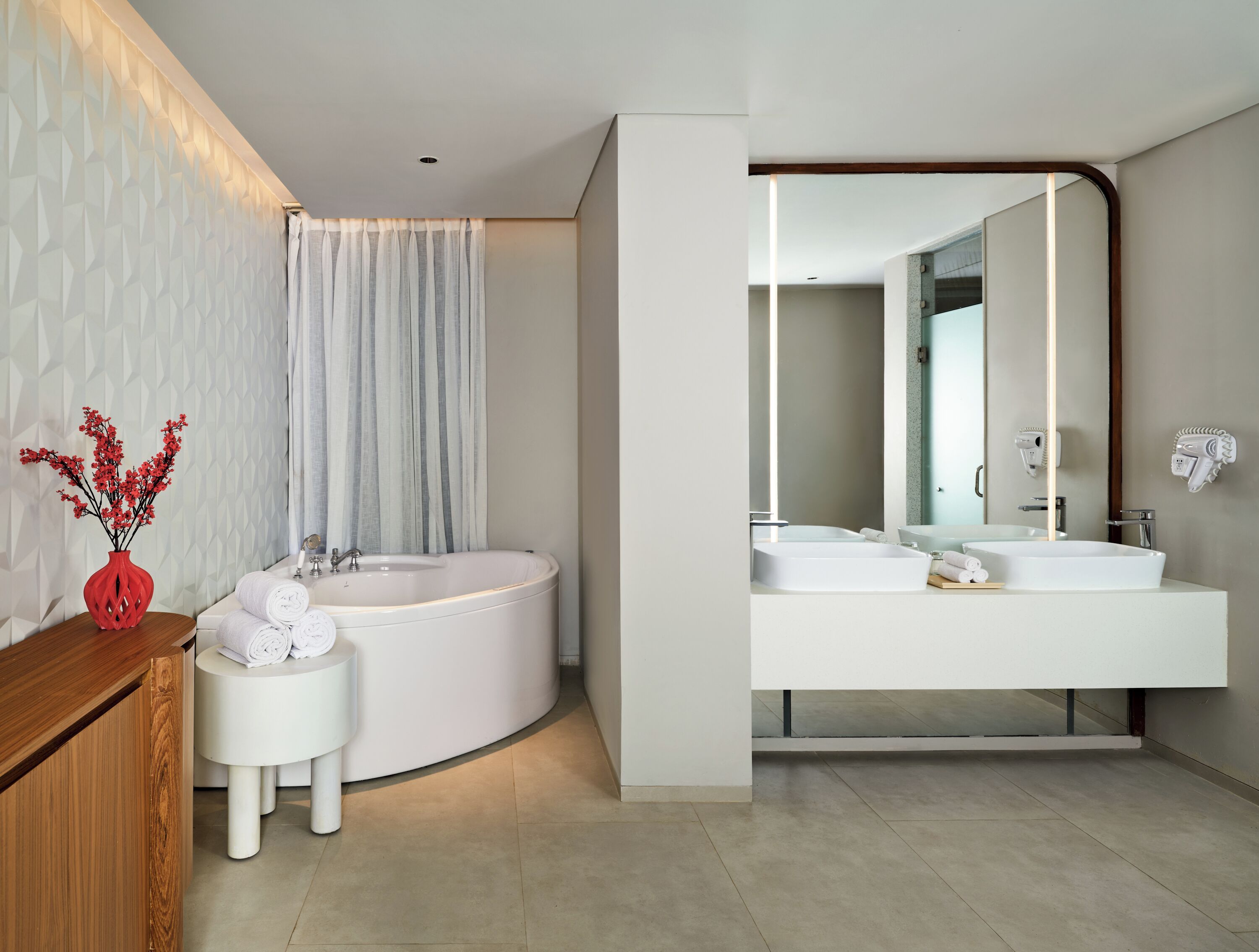A modern bathroom with a freestanding bathtub, a vanity with a mirror, and a wooden side table with towels.