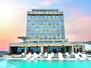 A modern hotel with a pool area, sun loungers, and umbrellas. - Swosti Premium Beach Resorts Puri (Brahmagiri)