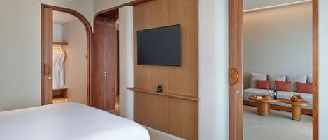 A modern hotel room with a large bed, a flat-screen TV mounted on the wall, a wooden wardrobe, and a seating area with a sofa and a small table.