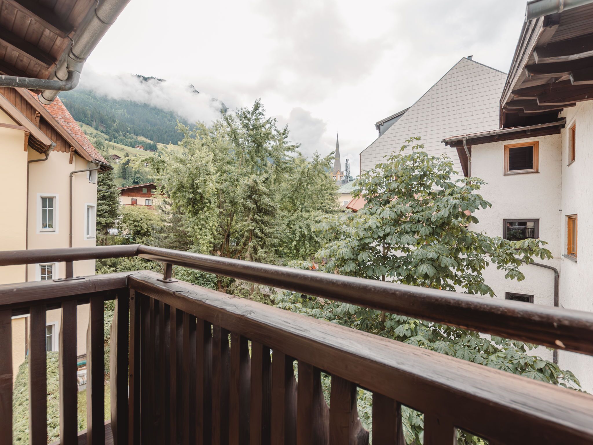 Un balcon doté d’une balustrade en bois, donnant sur un village aux bâtiments traditionnels, avec une montagne en arrière-plan.