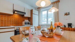 A modern kitchen with a dining area, featuring a wooden table set for a meal, a microwave, and a window with a view of the outdoors.