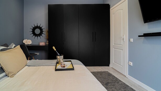 Ein Schlafzimmer mit einem Bett, einem Kleiderschrank, einem an der Wand befestigten Fernseher und einem Nachttisch mit Flasche und Gläsern.