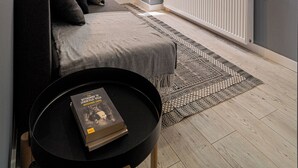 Ein modernes Schlafzimmer mit grauem Sofa, einem schwarzen Couchtisch, einer großen Pflanze und einem an der Wand befestigten Fernseher.