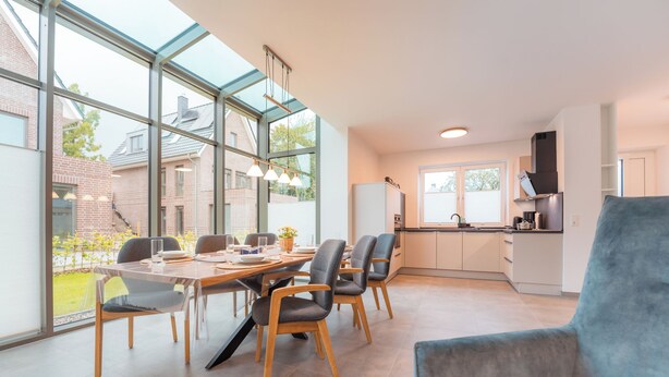 Eine moderne Küche mit einem großen Fenster, einem Essbereich mit Tisch und Stühlen sowie einem blauen Sessel.