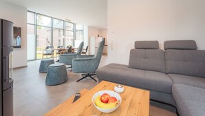 Ein modernes Wohnzimmer mit einem grauen Sofa, blauen Sessel und einem Couchtisch mit Obst.