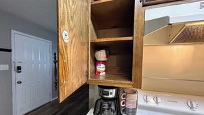 A kitchen with a white stove, a coffee maker, and a stack of mugs. - Affordable & Cozy Near the Base is set in Lawton. Both free WiFi and parking on-site are accessible at the apartment free of charge! (Lawton)