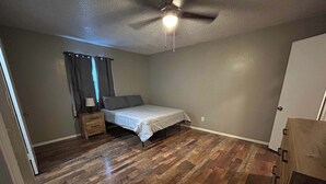 A bedroom with a bed, wooden flooring, a nightstand, a ceiling fan, and a door. - Affordable & Cozy Near the Base is set in Lawton. Both free WiFi and parking on-site are accessible at the apartment free of charge! (Lawton)