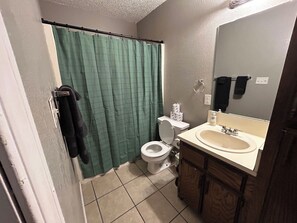 A small bathroom with a toilet, sink, and green shower curtain. - Affordable & Cozy Near the Base is set in Lawton. Both free WiFi and parking on-site are accessible at the apartment free of charge! (Lawton)