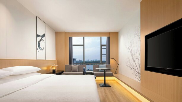A modern hotel room with a large bed, a seating area with a table, a TV, and a view of the city through large windows. - Fairfield by Marriott Chuzhou Railway Station (Chuzhou)