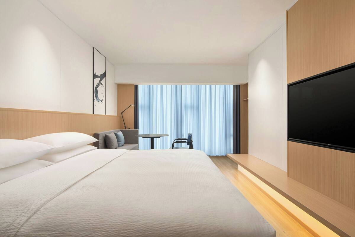 Ein modernes Hotelzimmer mit einem großen Bett, einem Flachbildfernseher, einem Schreibtisch und einem Sessel.