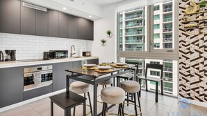 A modern kitchen with dark cabinets, white tiles, and a large window overlooking a residential building. - Beautiful Apartment with gym and  amazing Pool (Miami)