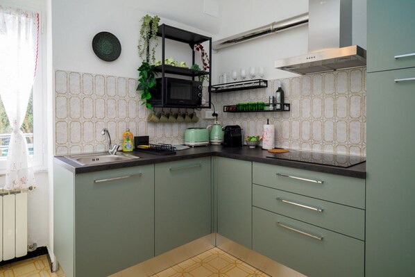 Une cuisine équipée d’un four à micro-ondes, d’un évier et de meubles de rangement verts.