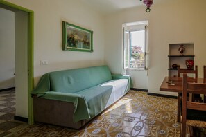 Une pièce avec un canapé vert, une petite table entourée de chaises, une fenêtre donnant sur un beau paysage et un sol à motifs.