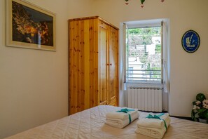A bedroom with a bed, a wooden wardrobe, a window with a view, and a framed picture on the wall.