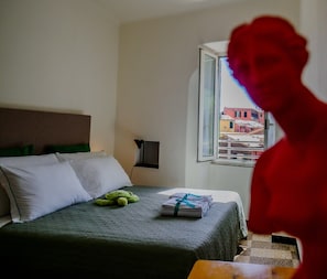 Une chambre d’hôtel avec un lit, des oreillers, une table de chevet, une lampe et une fenêtre donnant sur des immeubles.