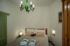 Ein ordentlich bezogenes Bett mit einer gesteppten Decke, zwei Kissen mit einem Blumenmuster, ein kleiner Nachttisch mit einer Lampe und eine grüne Wand.