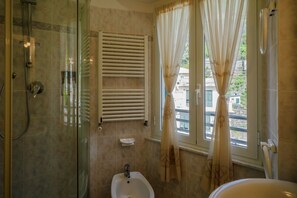 Ein Badezimmer mit Duschkabine, Bidet, Handtuchhalter und einem fensterbepflanzten Fenster.