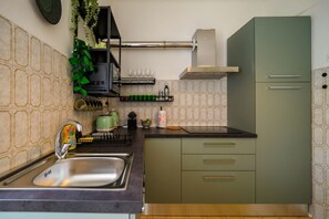 A kitchen with a sink, green cabinets, a stainless steel range hood, and a backsplash with a geometric pattern.