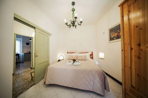 Ein Schlafzimmer mit einem Bett, einem Holzschrank, einer Chandelier, einem Gemälde an der Wand und einer Tür zu einem Badezimmer.