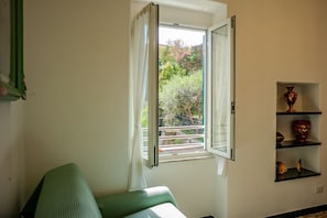 Ein Zimmer mit Fenster, einem grünen Sessel und einem Regal mit Dekoration.