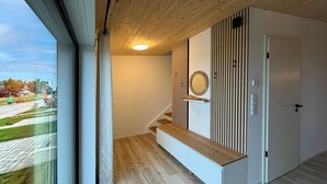 Un interior moderno con una escalera de madera, una puerta blanca y vistas al exterior.