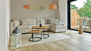 Un salón moderno con un sofá, una mesa redonda de centro, una lámpara colgante y vistas al exterior.