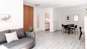Un salon moderne avec un canapé gris, un coin repas avec une table et des chaises, et une cuisine en arrière-plan.