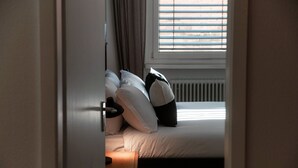 Une chambre à coucher avec un lit, des oreillers, une table de chevet et une fenêtre avec des stores.