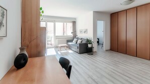 Un salon moderne avec une table à manger en bois, un canapé gris et une grande fenêtre.
